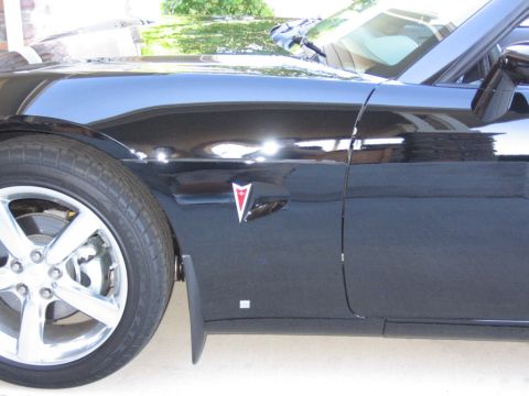 1995 Ford Bronco - Close-up of a black car's fender and door, showing the wheel and a Pontiac emblem.