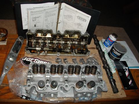 1989 Ford Probe - Disassembled engine parts including a cylinder head and camshaft are laid out with a service manual.