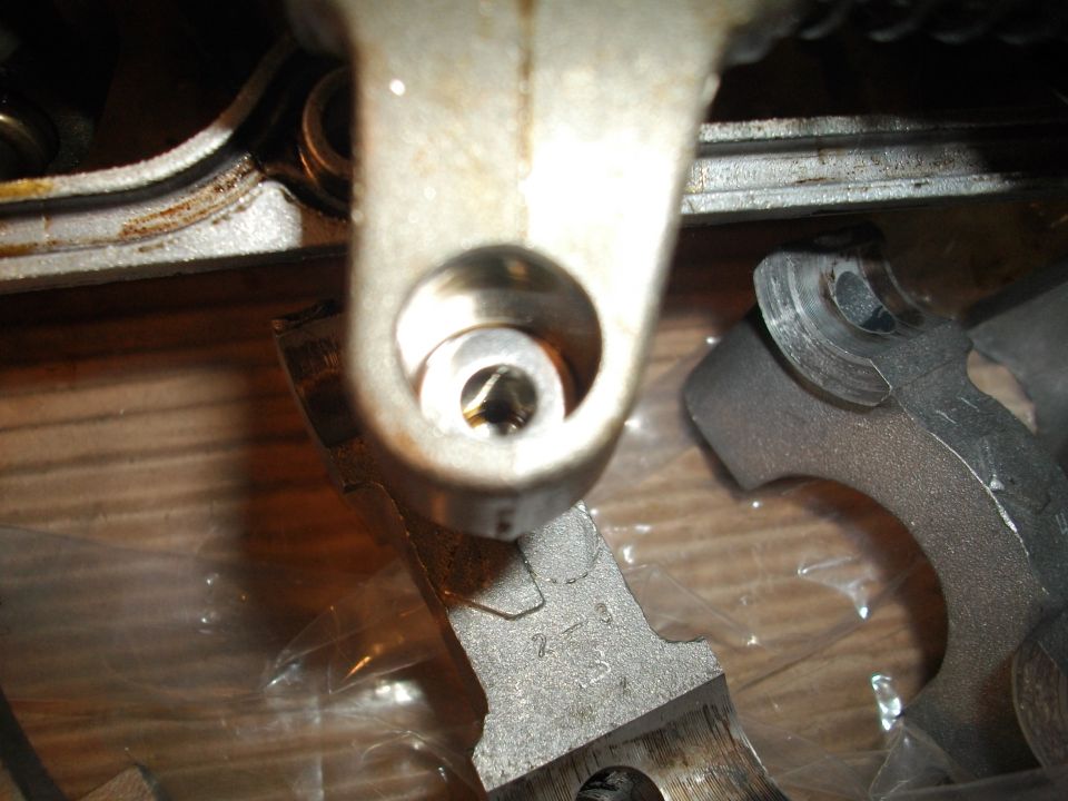 Close-up of engine valve train components, possibly rocker arms and shims. Some parts have numbers stamped on them