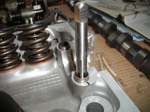 1989 Ford Probe - A tap tool is shown being used on an engine cylinder head, with valve springs and a camshaft in the background.
