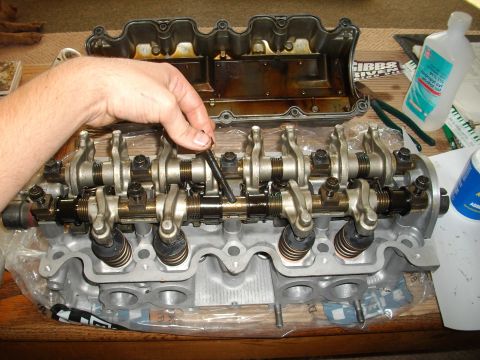 1989 Ford Probe - Close-up of a disassembled engine cylinder head with a hand adjusting a component.