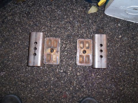1989 Ford Bronco - Two pairs of metal suspension components are laid out on a dark, asphalt surface.