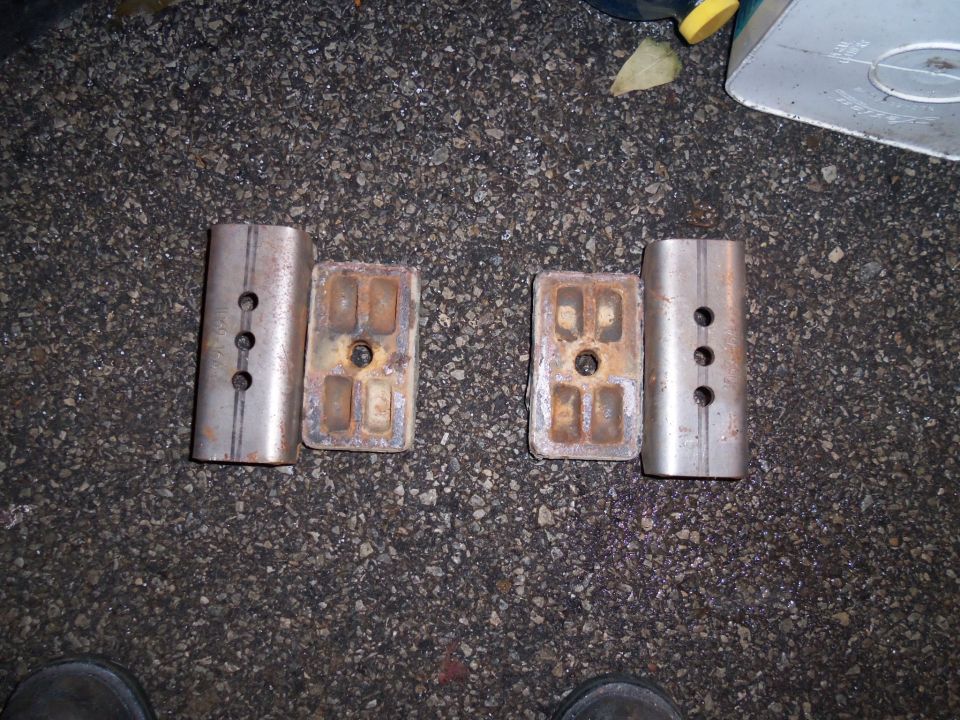 Two pairs of metal suspension components on asphalt