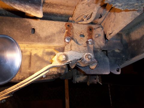 1989 Ford Bronco - Detail of a vehicle's rusty rear suspension components, including a linkage and leaf spring, viewed from underneath.