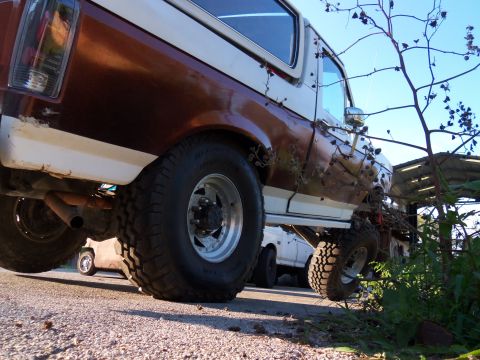 1989 Ford Bronco - Rear view of a lifted, two-tone Ford Bronco with off-road tires and visible rust.