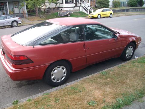 1989 Ford Probe - A red 1989 Ford Probe is parked on a residential street next to a yellow hatchback.