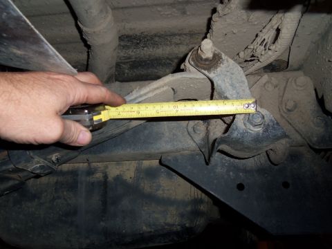 1989 Ford Bronco - A hand holds a tape measure to a vehicle's rear suspension component, indicating a measurement is being taken.