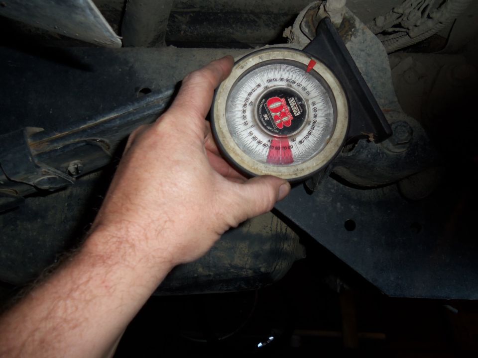 Hand holding an angle gauge against a vehicle's rear suspension component