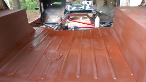 1978 Ford Bronco - The interior floor of a vehicle is coated in red-brown primer, revealing its ribbed metal construction and a central access panel.