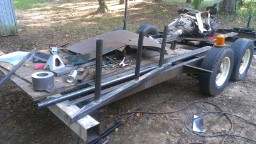 1978 Ford Bronco - A trailer frame is under construction, loaded with metal poles and various construction materials in an outdoor setting.