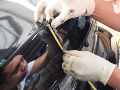 2003 Ford Crown Victoria - Gloved hands measure and mark a black car's trunk lid with tape measure during trim fitting.