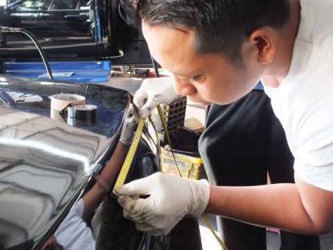 2003 Ford Crown Victoria - technician carefully marks a black sedan's trunk surface using a tape measure during installation.