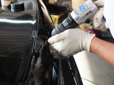 2003 Ford Crown Victoria - technician drills into the edge of a black car body panel with a cordless drill during trim mounting.