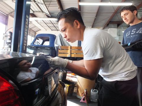2003 Ford Crown Victoria - worker applies a part to a black sedan's trunk while a coworker in a USA shirt observes.
