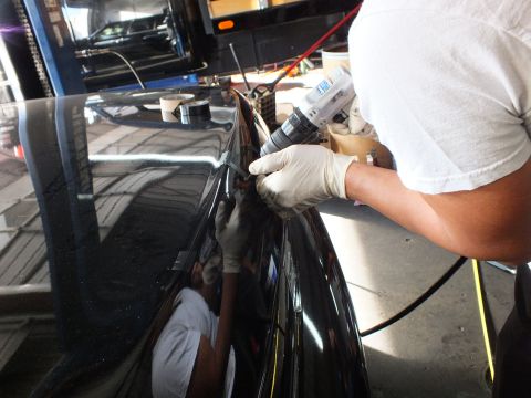 2003 Ford Crown Victoria - Hands in latex gloves operate a drill along the trunk edge of a glossy black sedan.
