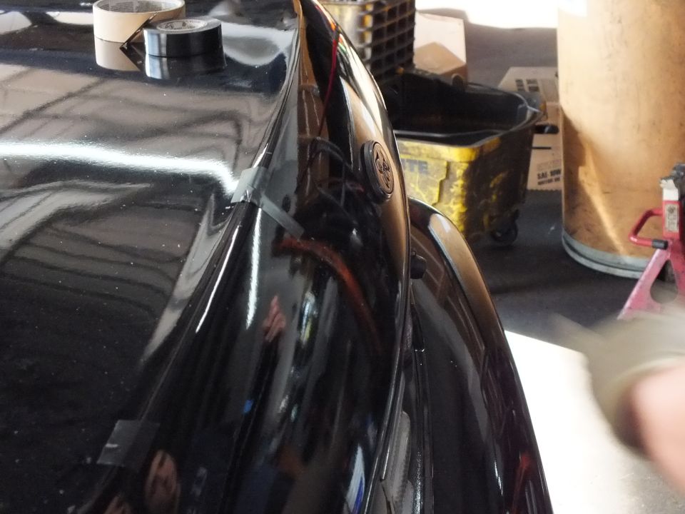 Close view of glossy black car rear trunk and quarter panel with tape and jack stand behind