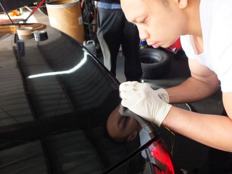 2003 Ford Crown Victoria - worker leans close to mark and wipe the trunk edge of a polished black sedan during trim install.