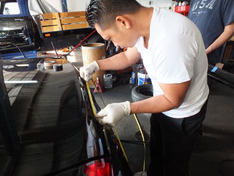 2003 Ford Crown Victoria - Worker applies a yellow guide line along the rear deck of a black sedan before drilling.