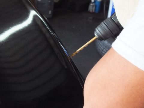 2003 Ford Crown Victoria - Detail of a power drill boring into the curved edge of a glossy black fender.