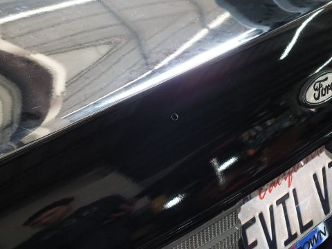 2003 Ford Crown Victoria - small mounting hole marks the glossy black trunk beside a Ford emblem.