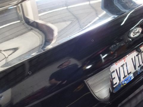 2003 Ford Crown Victoria - Two fresh mounting holes flank the rear deck of a black Ford near its plate.