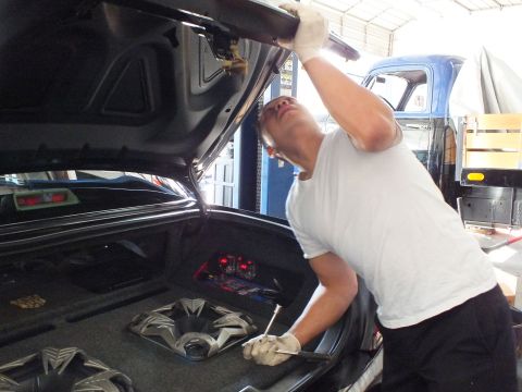 2003 Ford Crown Victoria - Technician works under a raised trunk lid above two speaker cones in the cargo area.