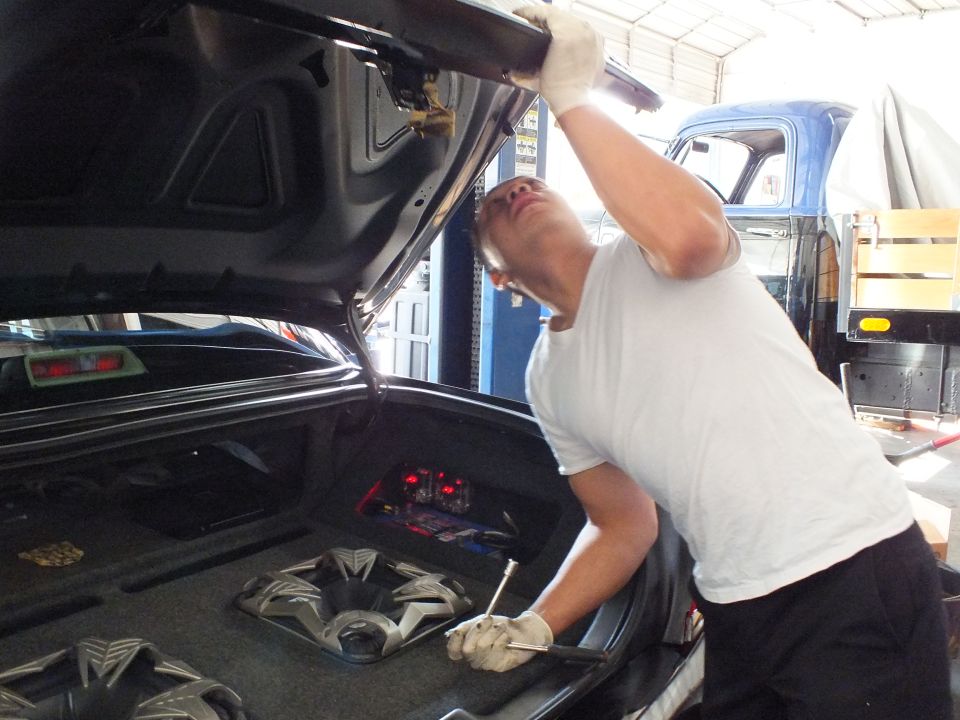 Man reaches inside open trunk of black sedan with subwoofer enclosures in garage