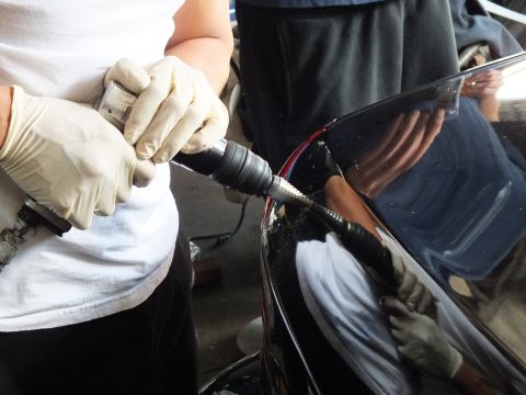 2003 Ford Crown Victoria - technician deburrs a drilled hole on a black panel using a flexible-shaft rotary tool.