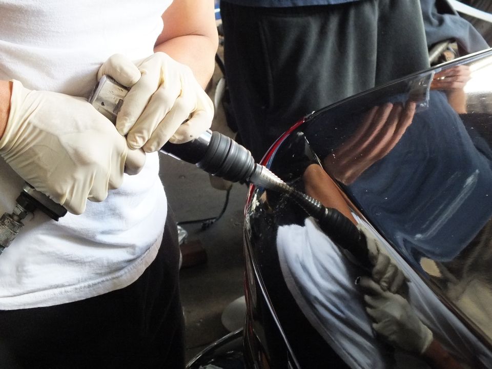 Gloved hands using rotary tool with flex shaft on edge of black car panel