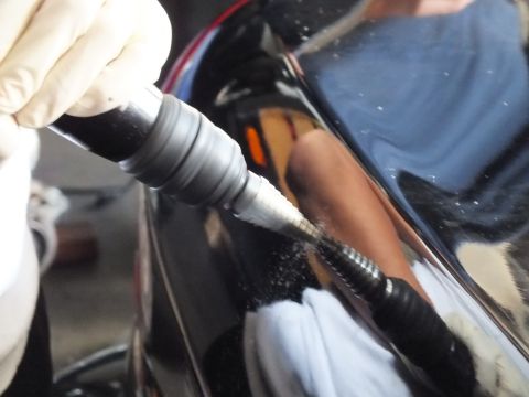 2003 Ford Crown Victoria - Close detail of a flexible-shaft tool finishing a bolt hole in a black body panel.