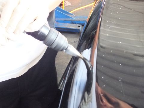 2003 Ford Crown Victoria - rotary tool works the rounded corner of a glossy black trunk amid grinding dust.