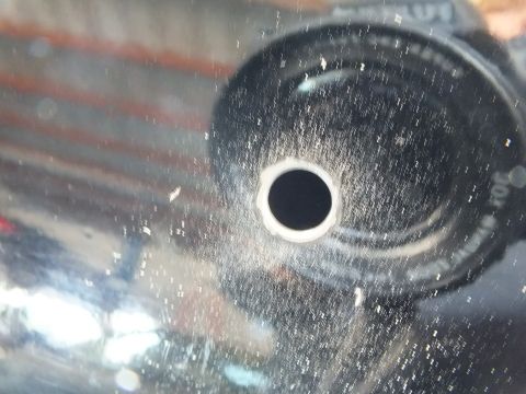 2003 Ford Crown Victoria - Macro view of a beveled mounting hole in a black surface coated with grinding dust.