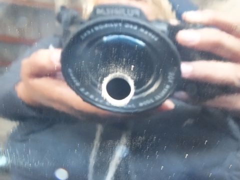 2003 Ford Crown Victoria - Reflection of a hand-held camera in a dusty black surface around a small hole.