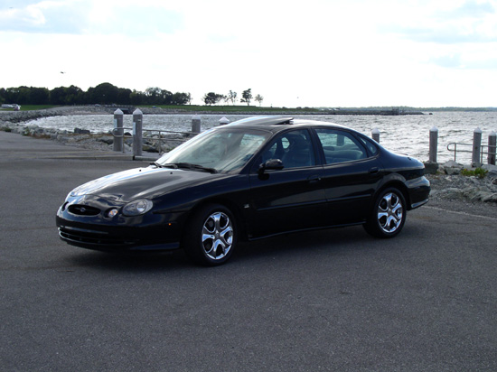 Black 1998 Ford Taurus parked near a waterfront with chrome wheels and a sunroof