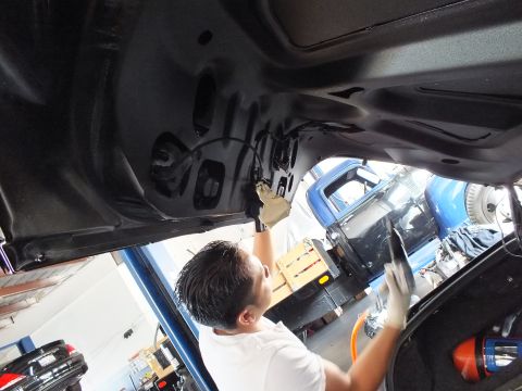 2003 Ford Crown Victoria - Technician reaches up to the inner structure of a raised black trunk lid in a garage.