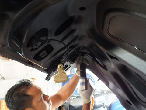 2003 Ford Crown Victoria - man fastens a spoiler bolt on the inner structure of an open black trunk lid.