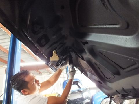 2003 Ford Crown Victoria - Gloved technician sprays a dark car's inner panel from below, blue vehicle and shop interior in background
