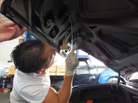 2003 Ford Crown Victoria - Technician in gloves braces a rod against the inner trunk panel of a dark car, shop shelving behind