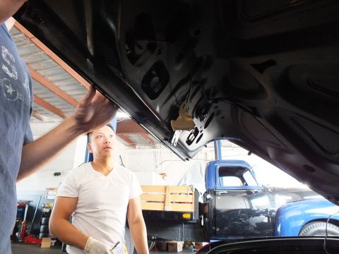 2003 Ford Crown Victoria - One worker holds the open decklid while another looks on, vintage blue pickup parked in background