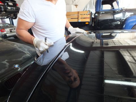 2003 Ford Crown Victoria - Worker runs a tool along the glossy decklid of a black BMW, kidney grille and blue truck visible