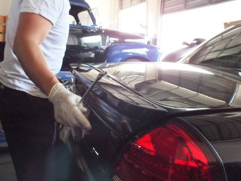 2003 Ford Crown Victoria - Gloved technician runs a tool along the trunk edge of a dark sedan, illuminated red taillight at right