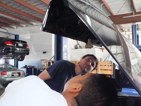 2003 Ford Crown Victoria - Two men look up at the inner panel of a raised dark trunk lid, a black sedan lifted in the background