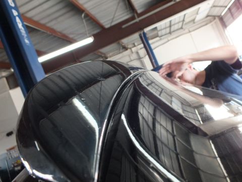 2003 Ford Crown Victoria - Reflective dark rear panel of a vehicle catches ceiling lights as a worker leans over it in the shop