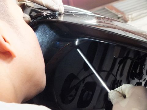 2003 Ford Crown Victoria - Technician guides a thin tool along the seam of a dark glossy vehicle panel, reflections across surface