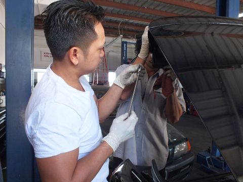 2003 Ford Crown Victoria - Pair of technicians using a hand tool at the rear of a black car inside a service shop