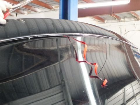 2003 Ford Crown Victoria - Orange double-sided tape strip peeled from a glossy black trunk lid in a garage