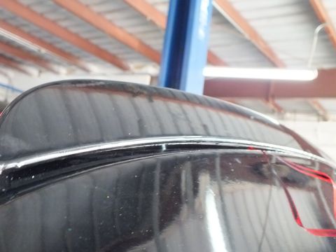 2003 Ford Crown Victoria - Detail of a black car's rear deck and trim line reflecting overhead shop lighting