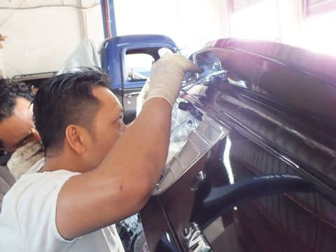 2003 Ford Crown Victoria - Technician works inside a black car's trunk area beside a vintage blue pickup truck