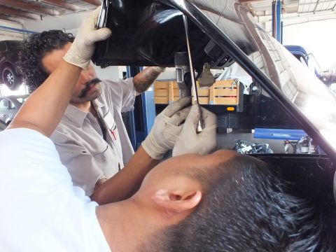 2003 Ford Crown Victoria - Technicians reach up into the underside of a black car's open trunk lid in the shop