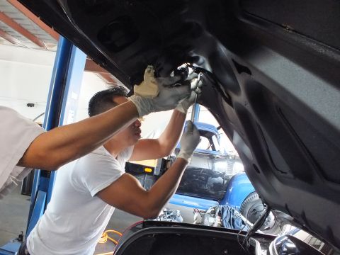 2003 Ford Crown Victoria - Technician reaches into the underside of a raised black trunk lid in a service bay